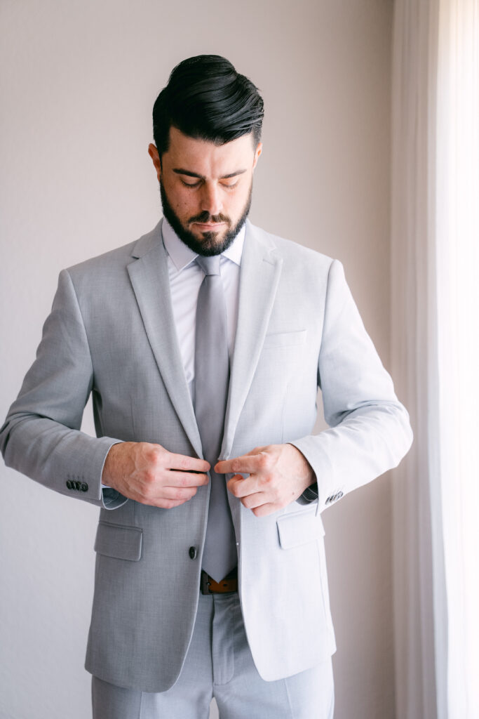 Chris buttoning his grey suit before the ceremony