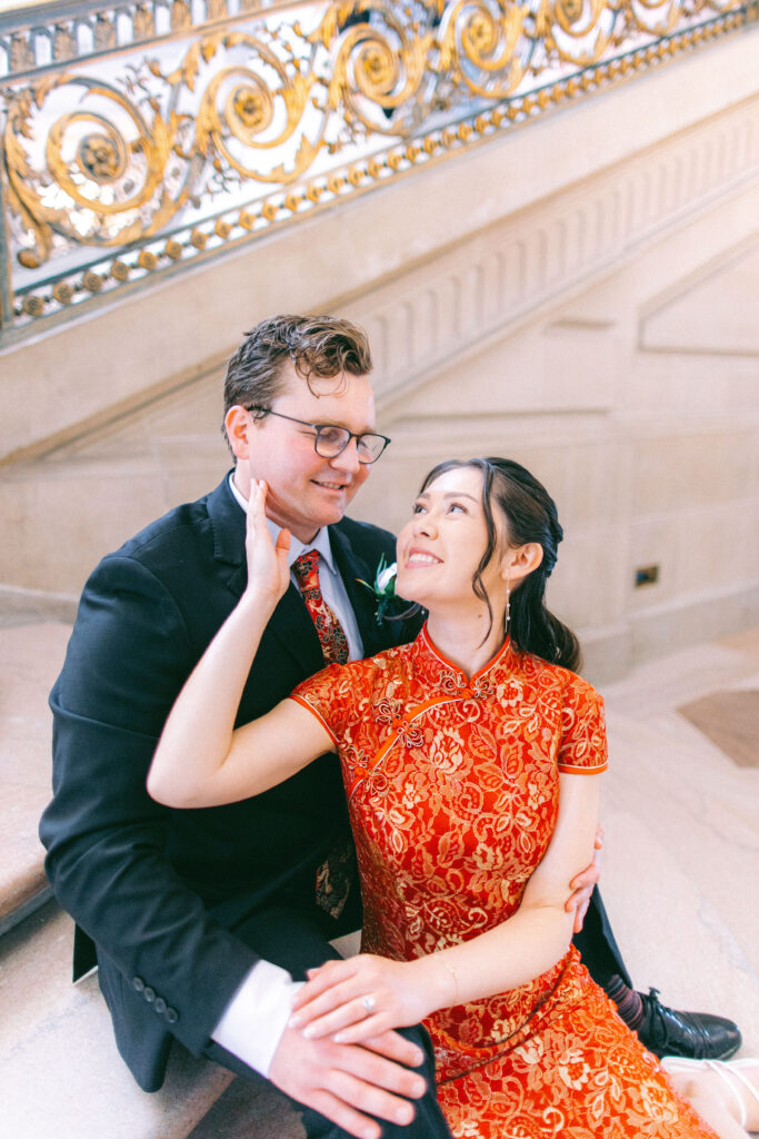Clare in a red Chinese dress sits with Matt on the stairs