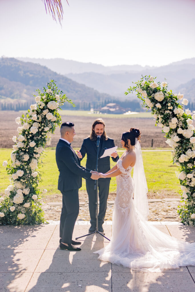Jocelyne and Cesar exchanging vows under a floral arch at Tuscany Escape