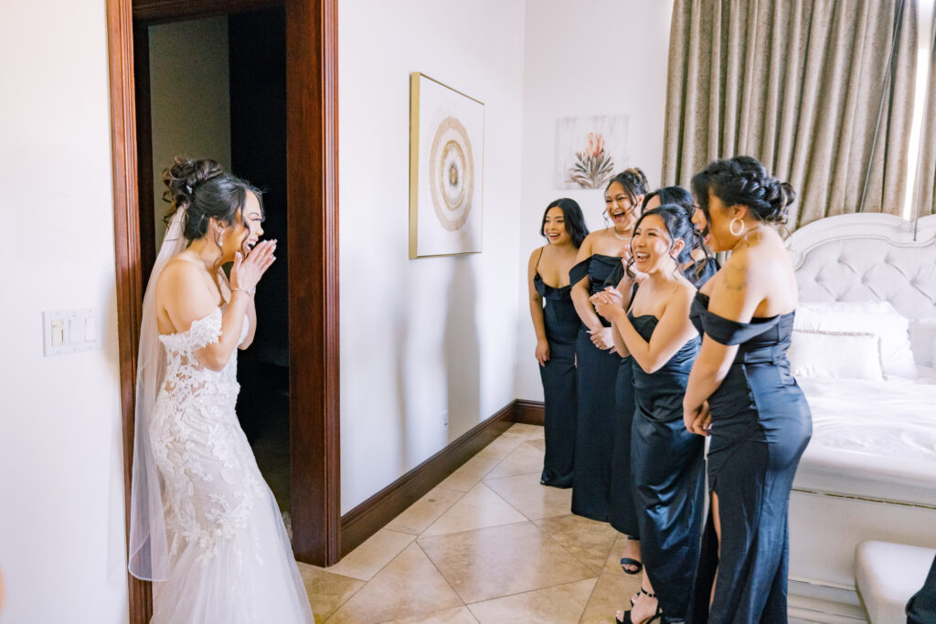 Jocelyne stepping through the door as her bridesmaids see her dressed up for the first time