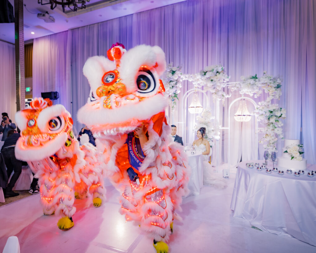 Two lion dancers moving through the reception room as Jocelyne and Cesar look on
