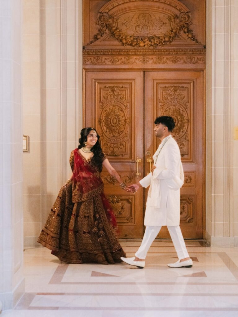 Radhika leads Vyshakh by the hand past an ornate door