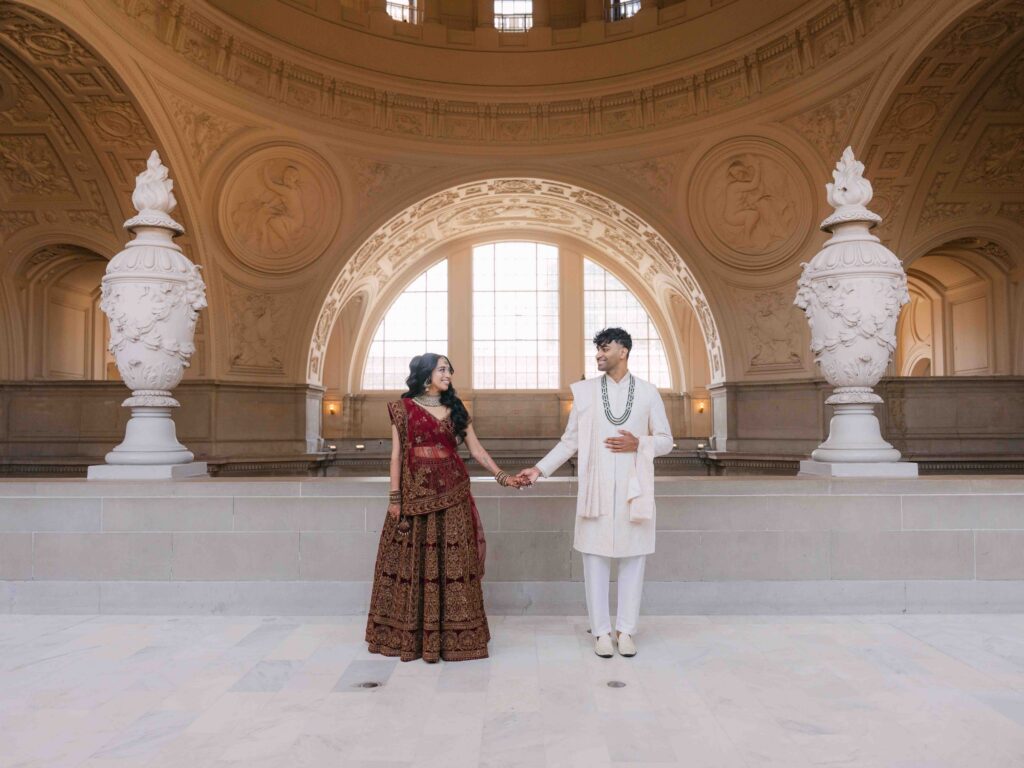 Indian wedding couple holding hands on the 4th floor gallery at San Francisco City Hall with grand architecture and soft natural light
